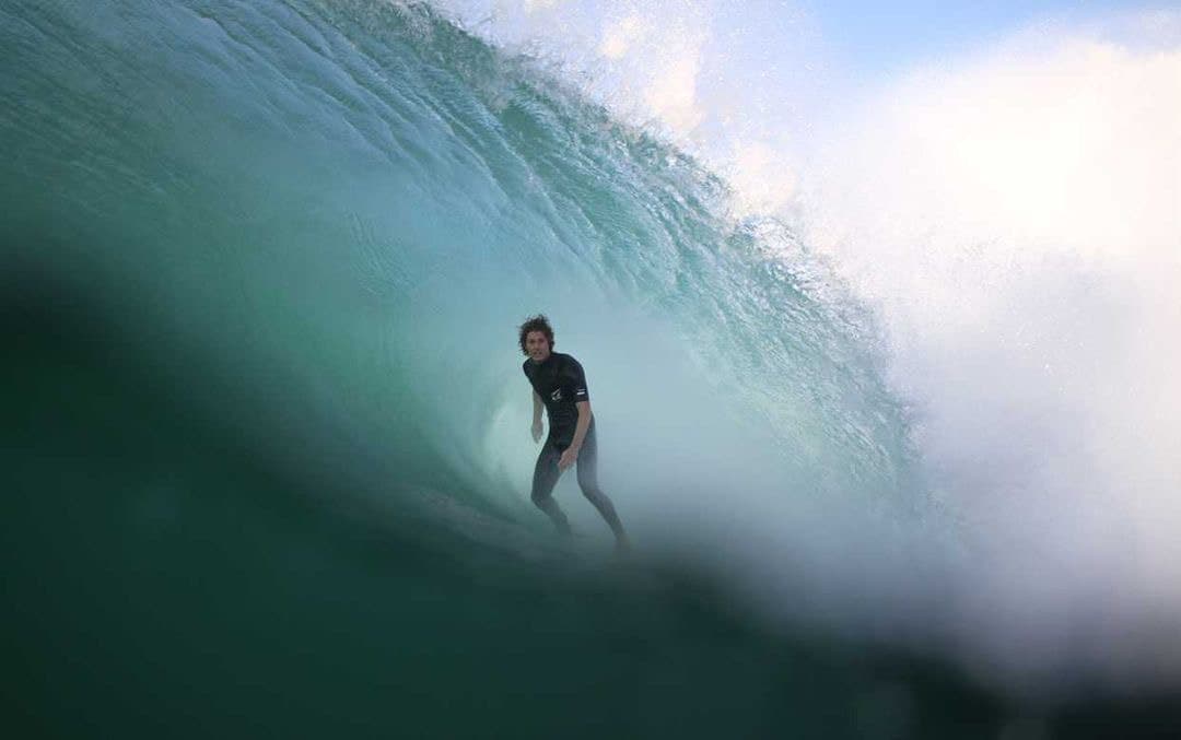 A bodyboarder holding a line inside a breaking blue wave.
