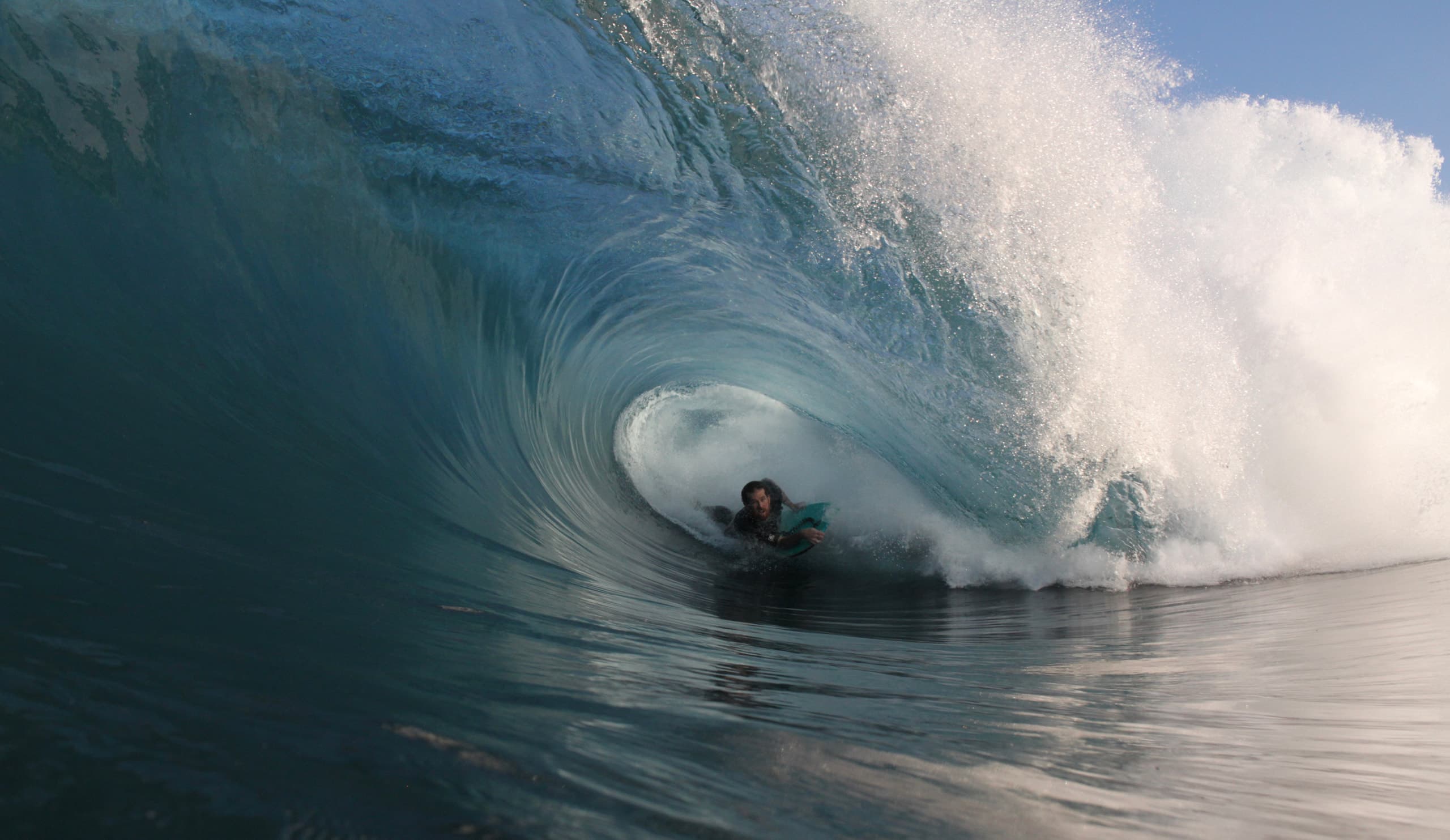 A bodyboarder holding a line inside a breaking blue wave.