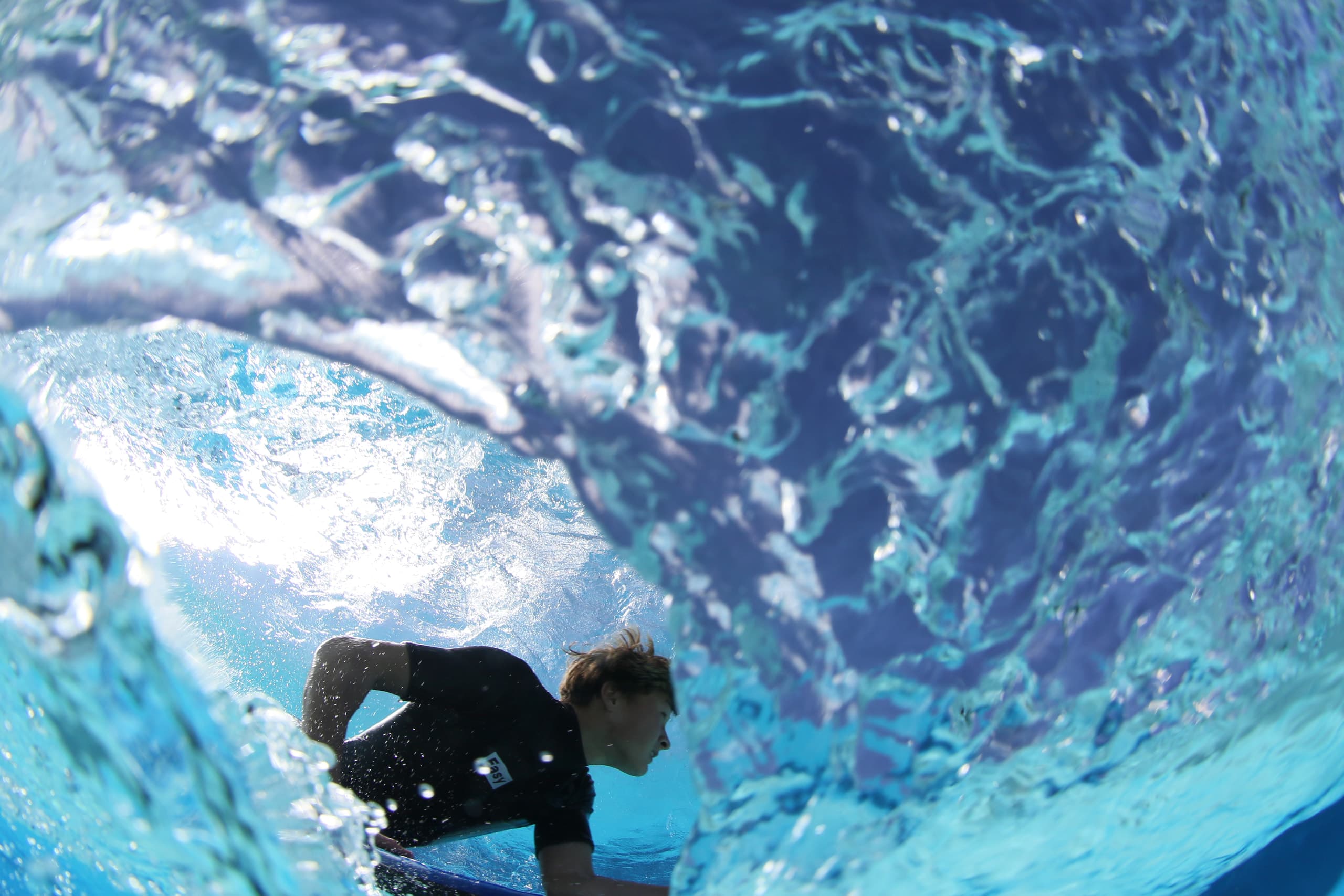 A bodyboarder seen through the translucent curve of a wave.