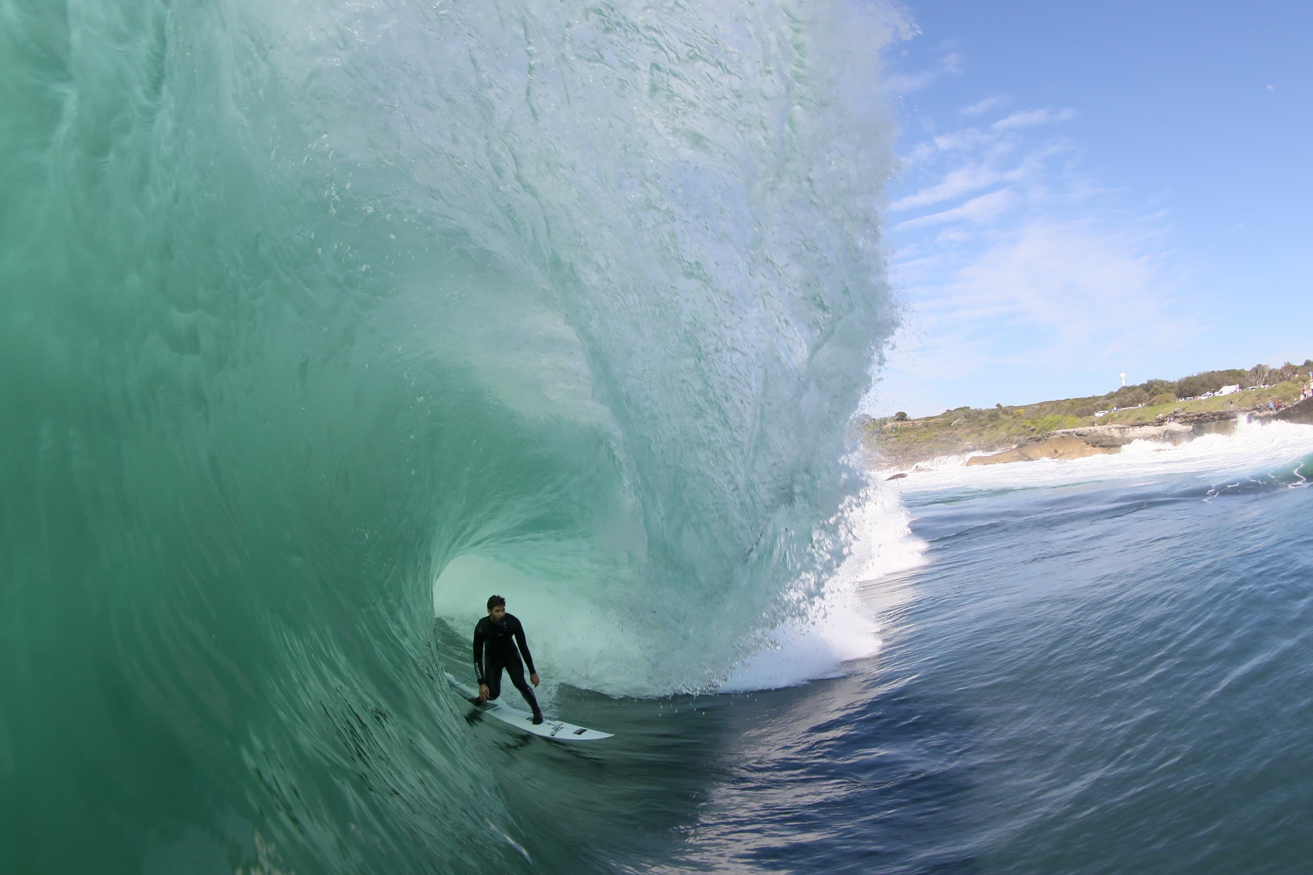 A surfer riding beneath the face of a large green wave.