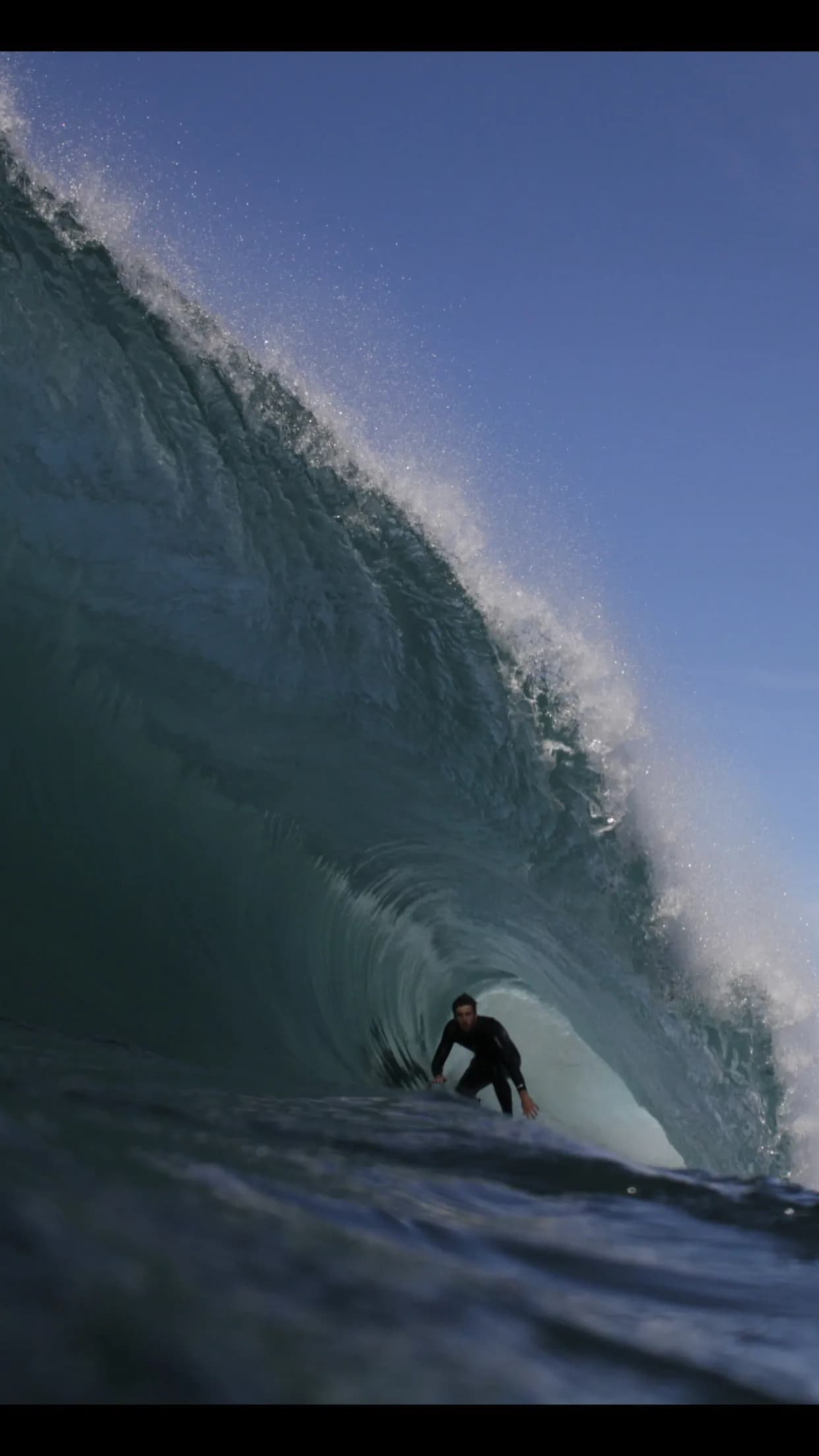 A bodyboarder framed vertically inside a steep blue wave.
