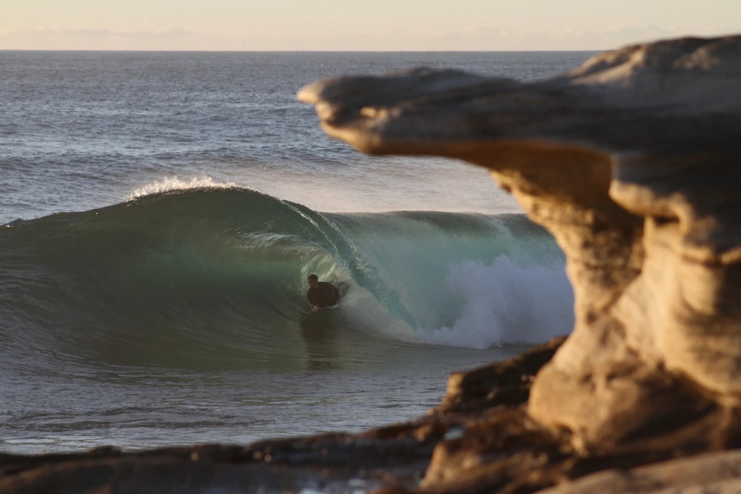 An empty green wave viewed through a sandstone opening.