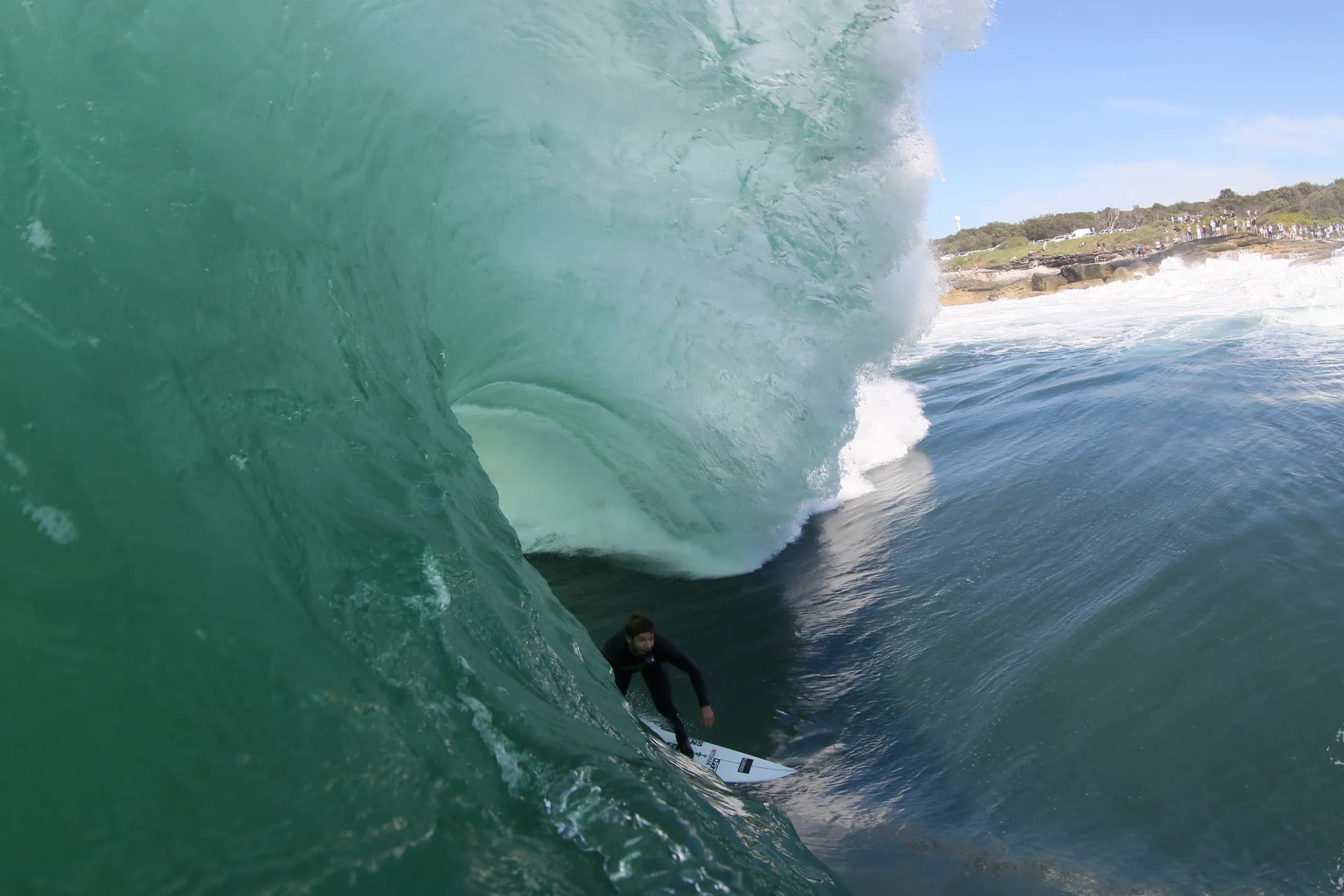 A surfer riding deep inside a large green wave.