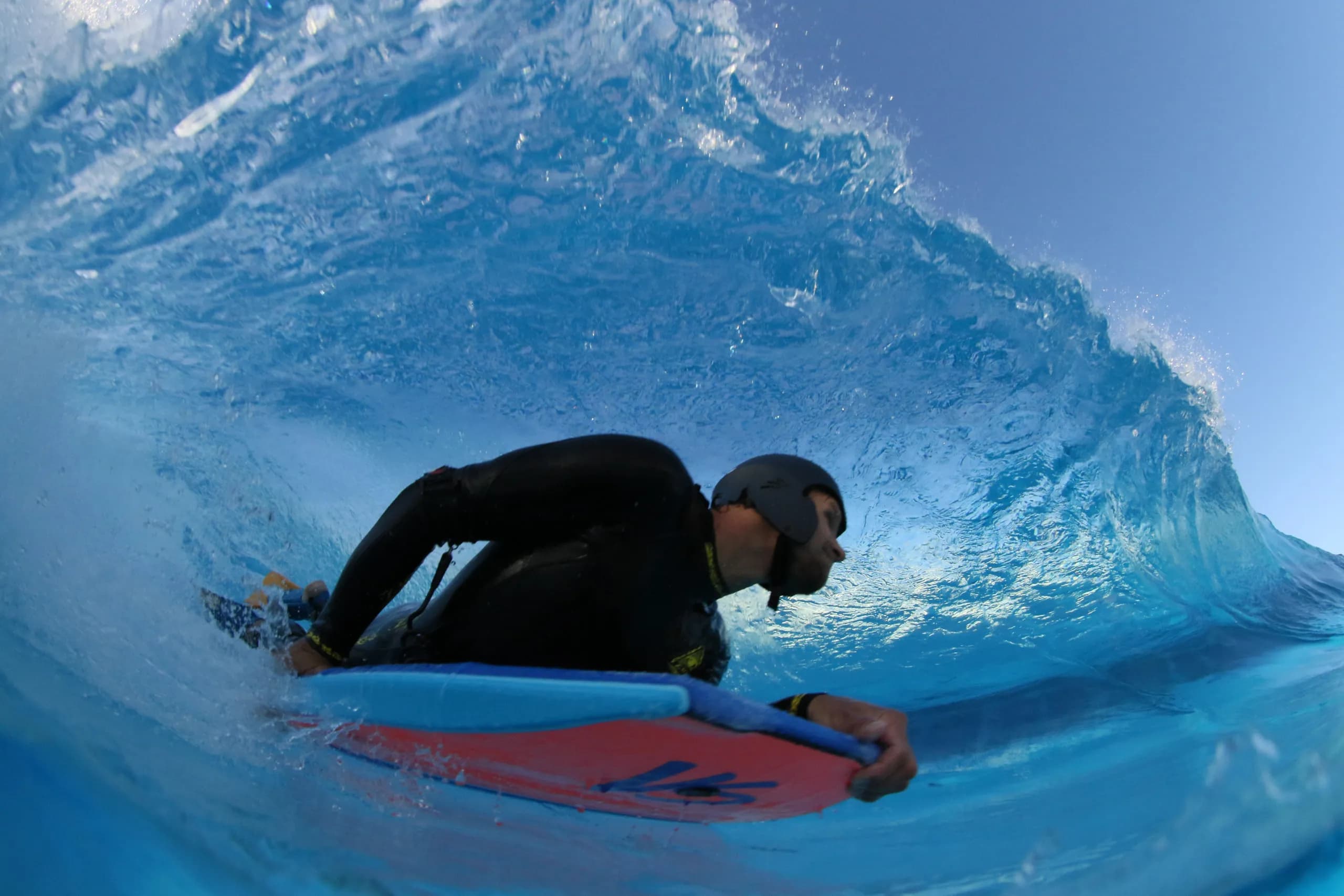 A bodyboarder with a red board inside a blue tube.