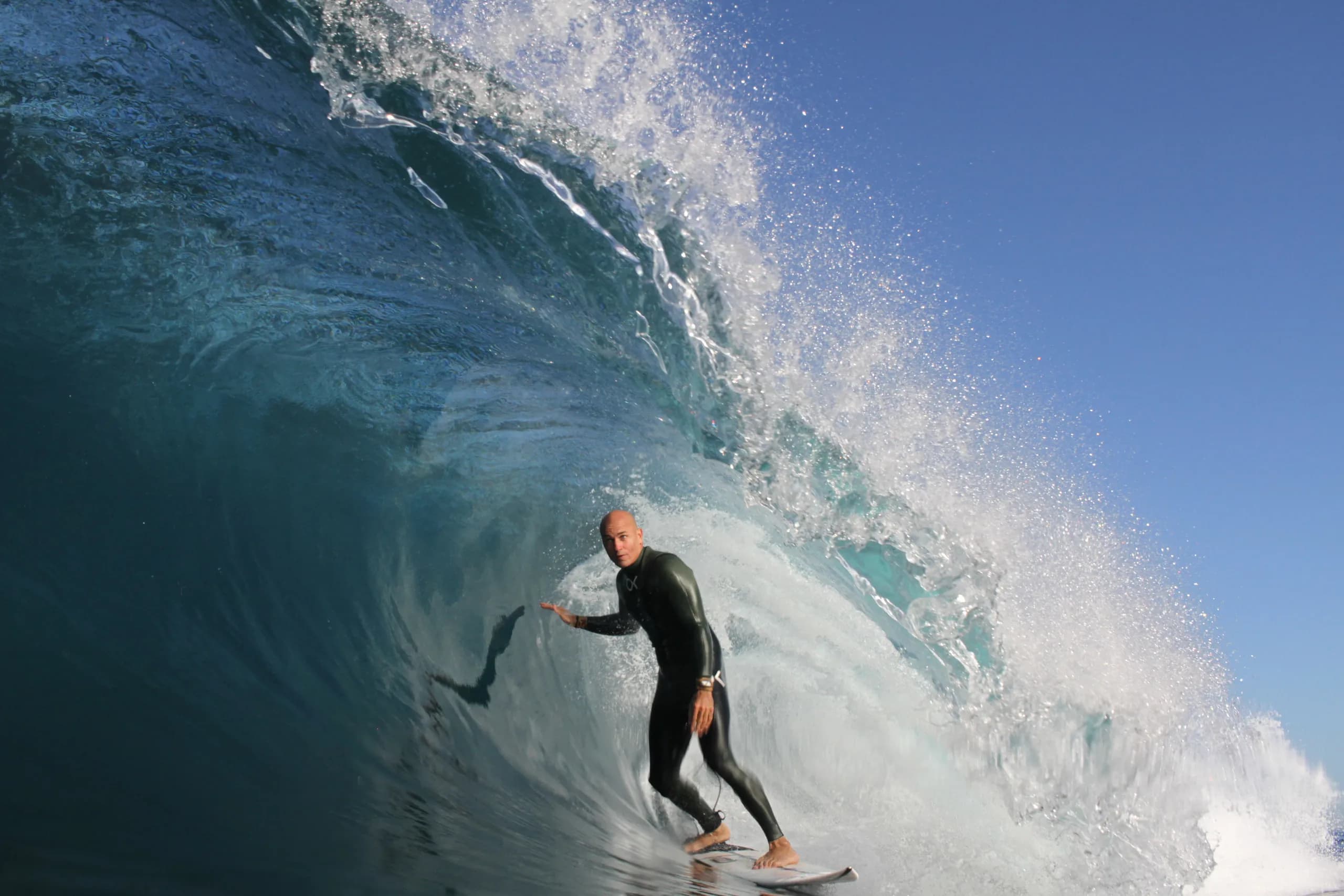 A surfer reaching toward the wall of a steep blue wave.