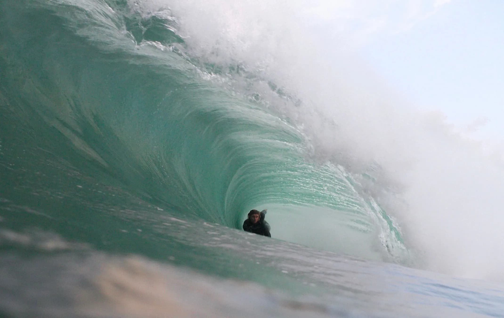 A bodyboarder riding beneath a curling green wave.
