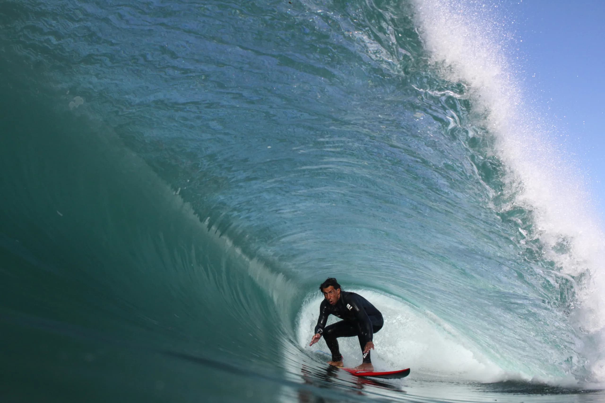 A surfer crouching beneath the face of a clear blue wave.