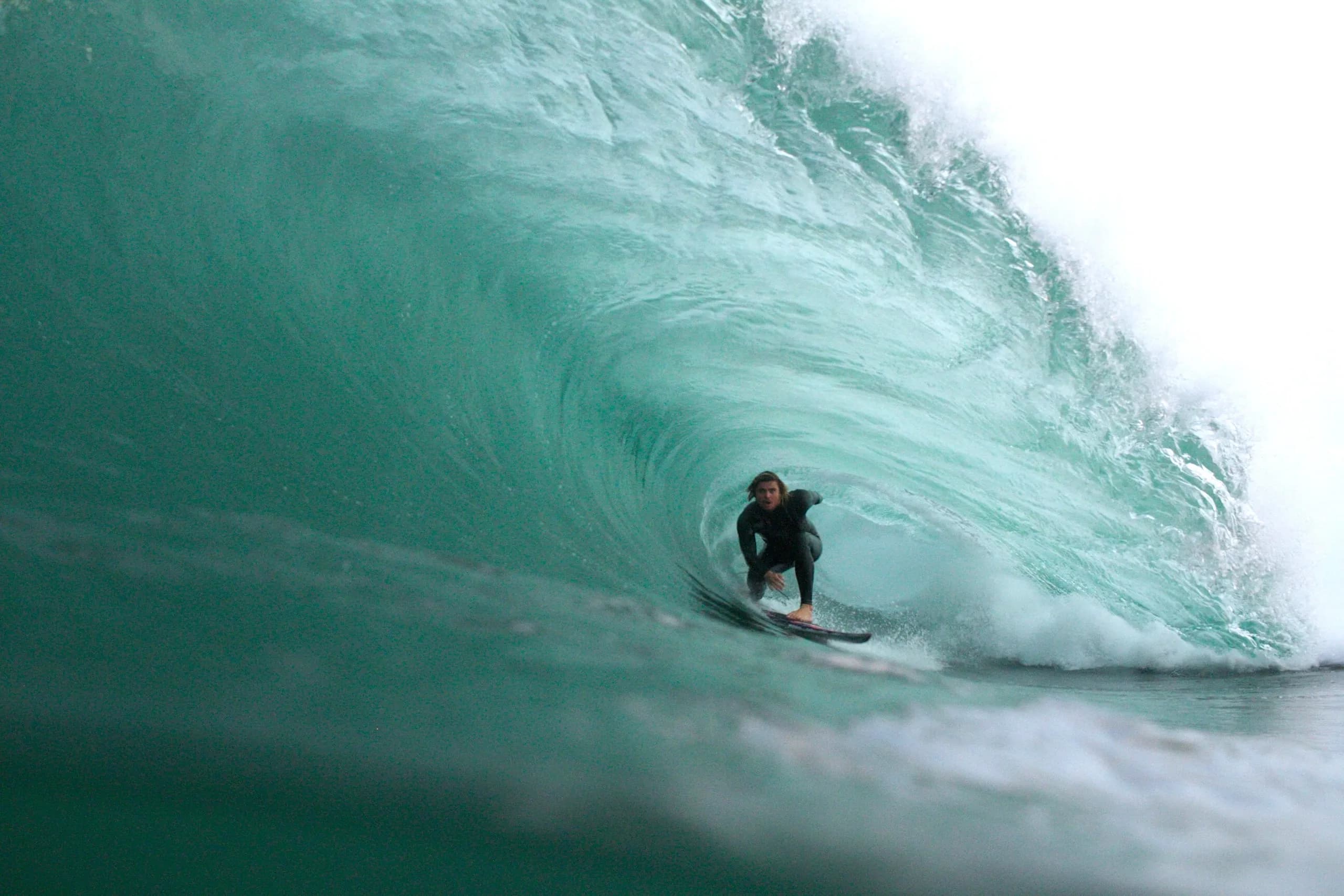 A surfer standing deep inside a green barrel.