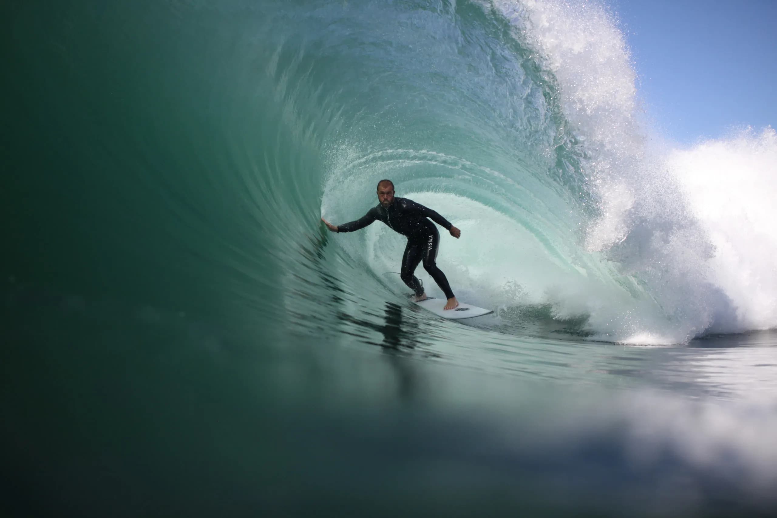 A surfer standing inside a bright turquoise barrel.