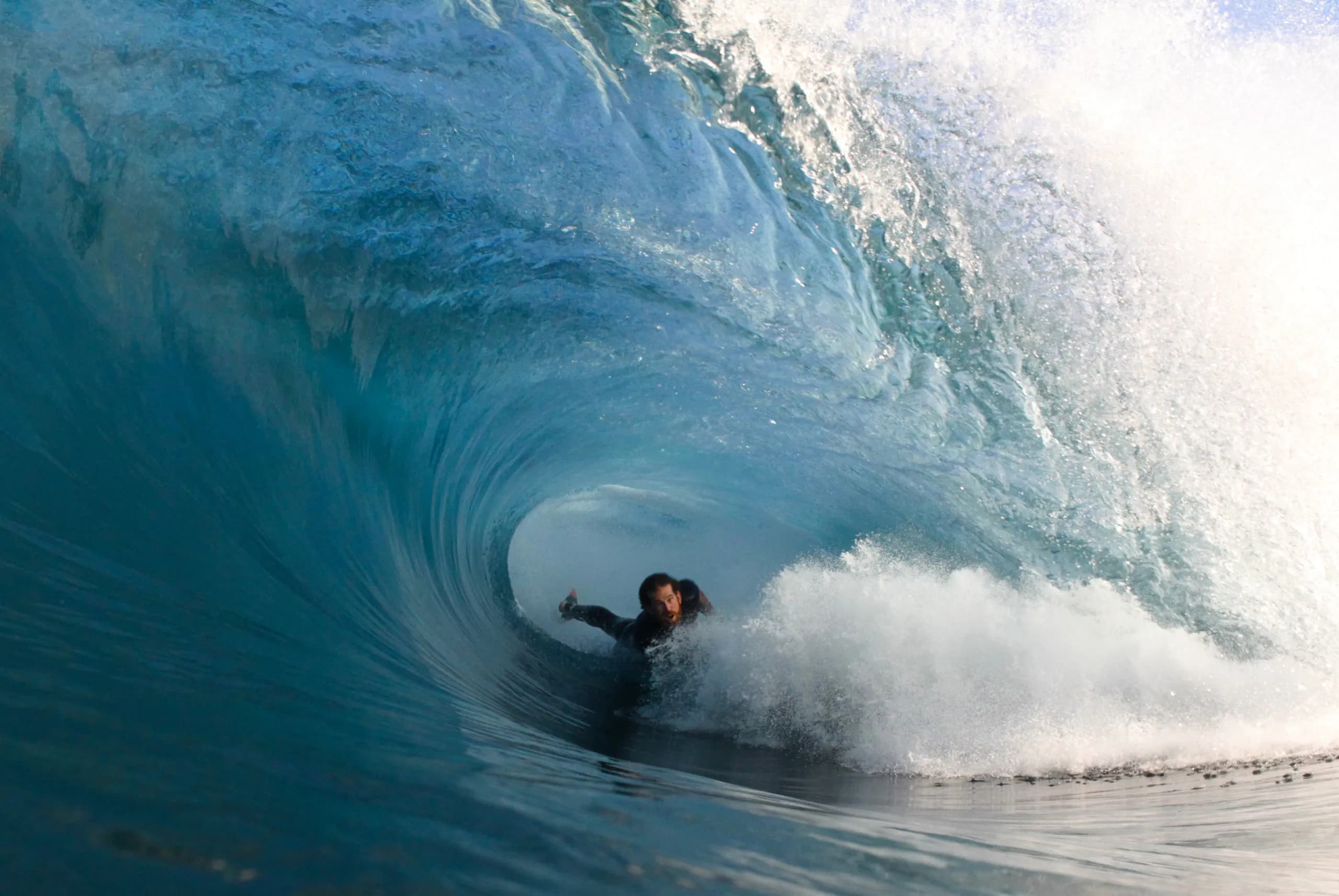 A bodyboarder driving across the face of a blue wave.