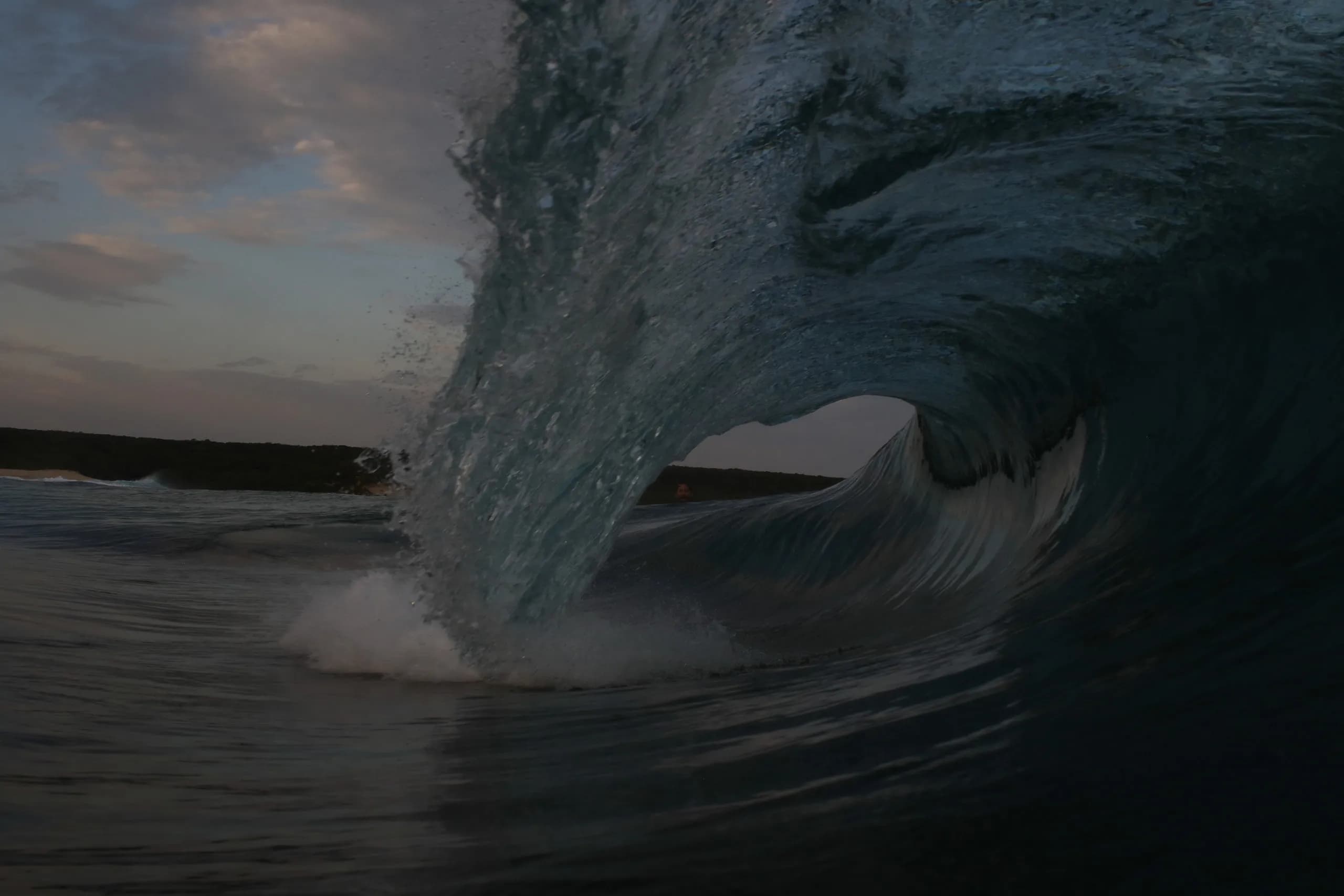 A dark wave breaking close to shore beneath an evening sky.
