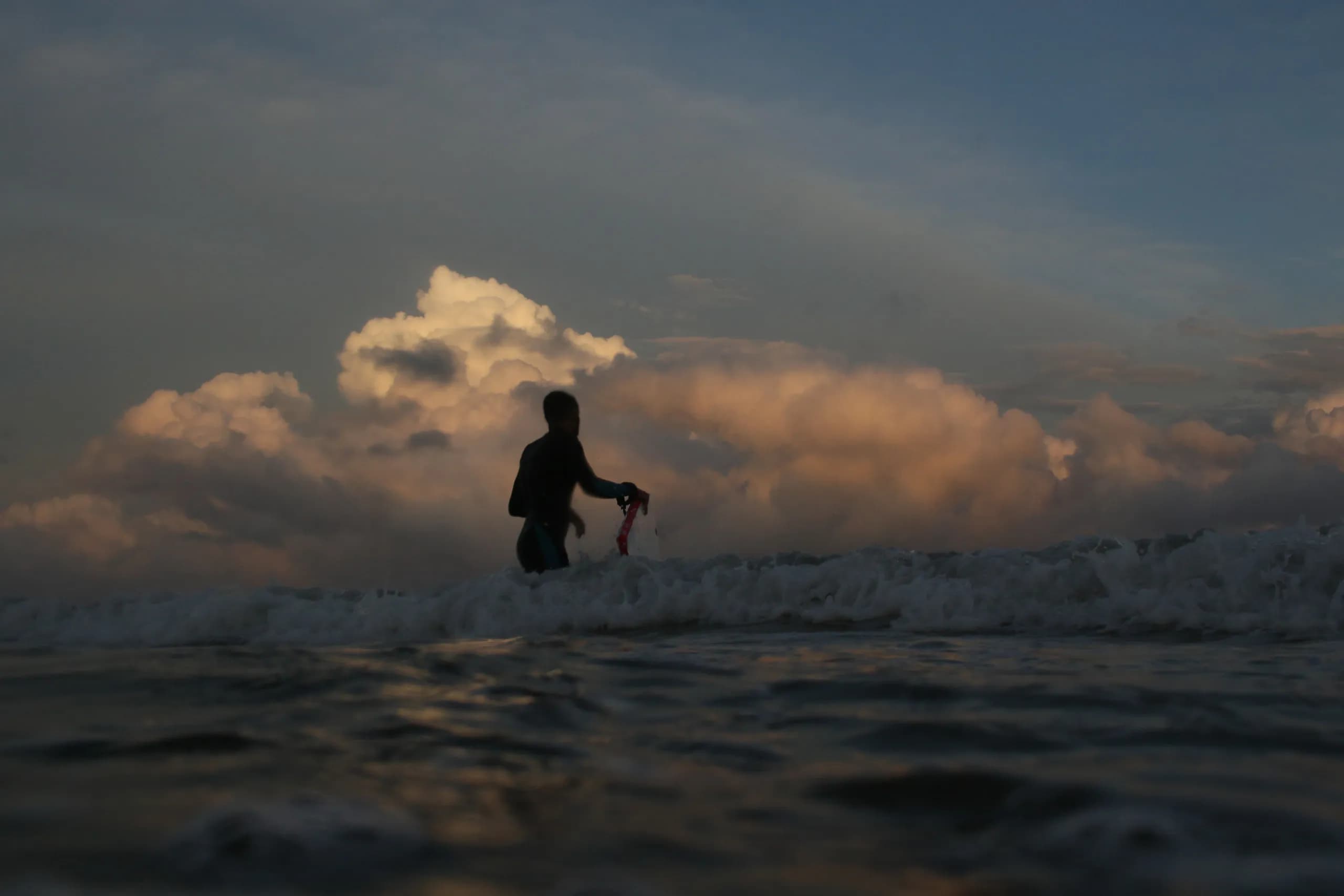 A surfer silhouetted against white water and evening clouds.