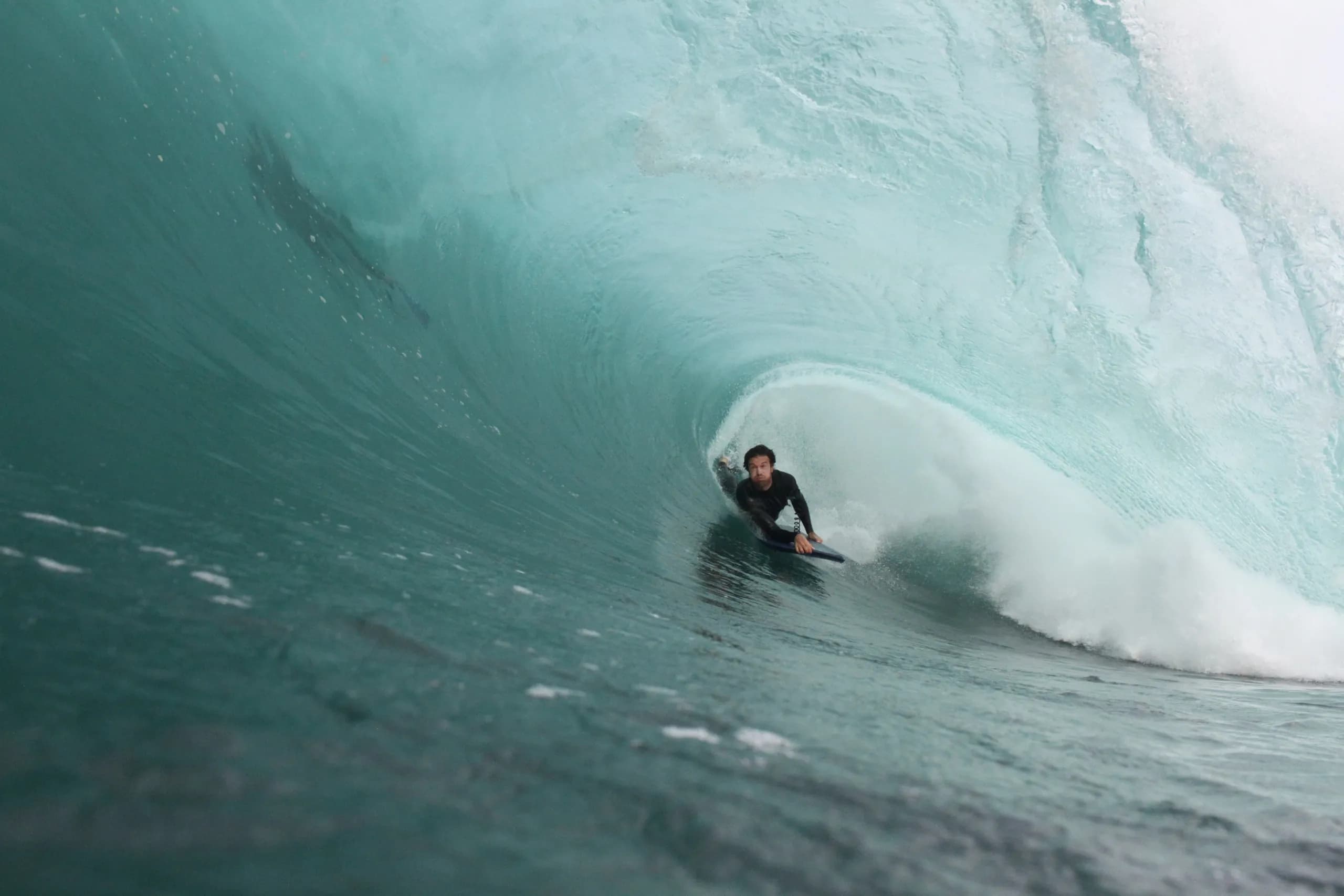 A surfer riding inside a pale green breaking wave.