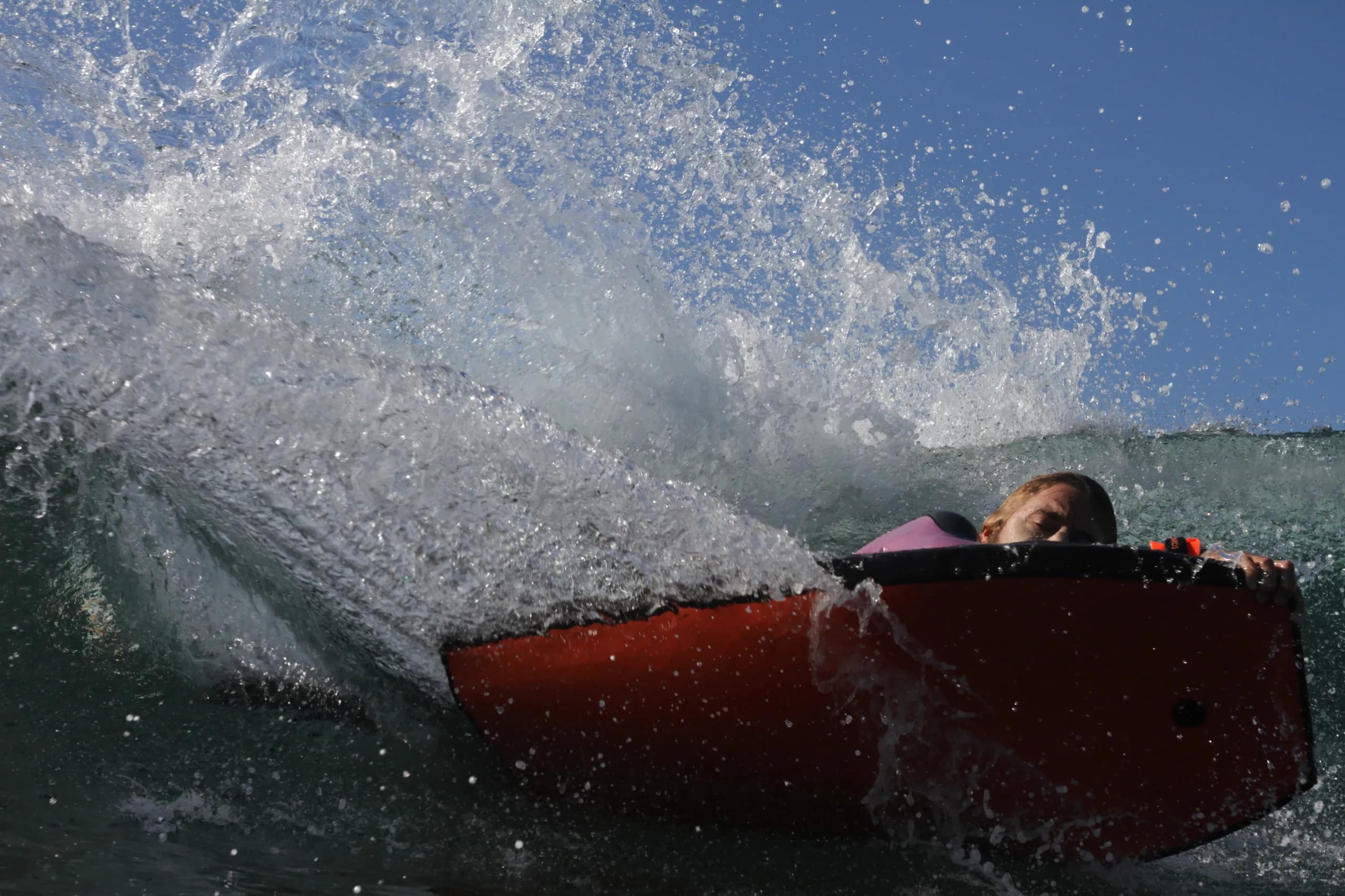 A bodyboarder holding a red board in turbulent shorebreak.