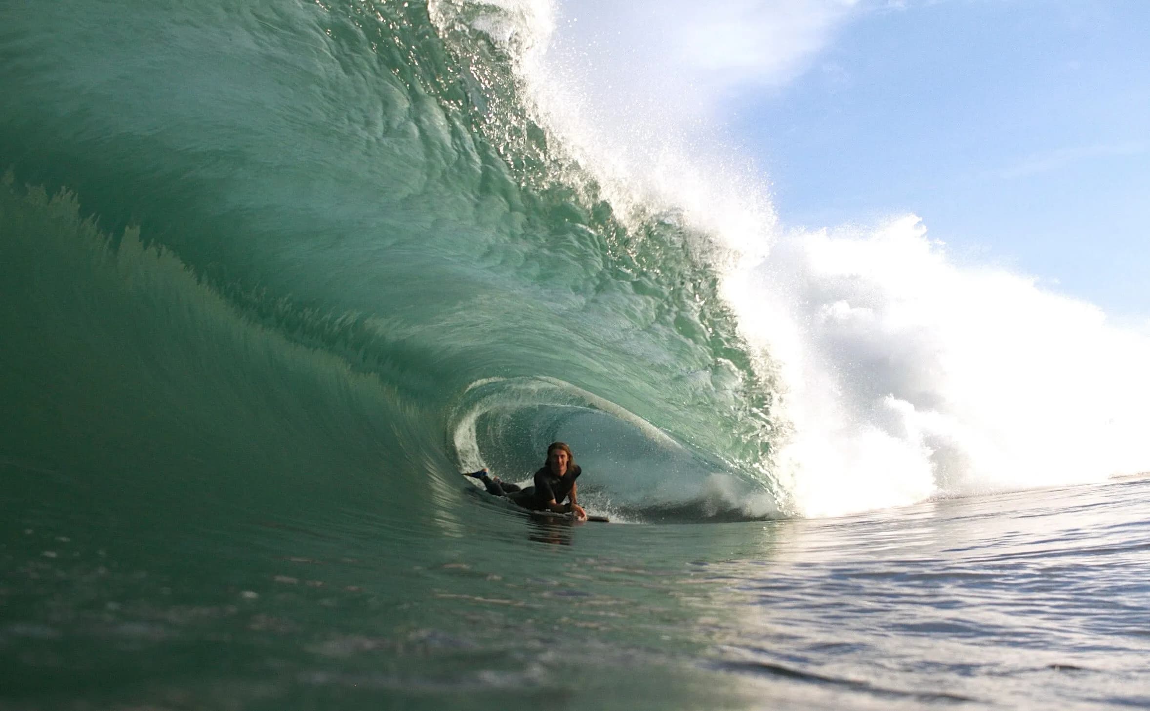 A bodyboarder tucked beneath the lip of a green wave.