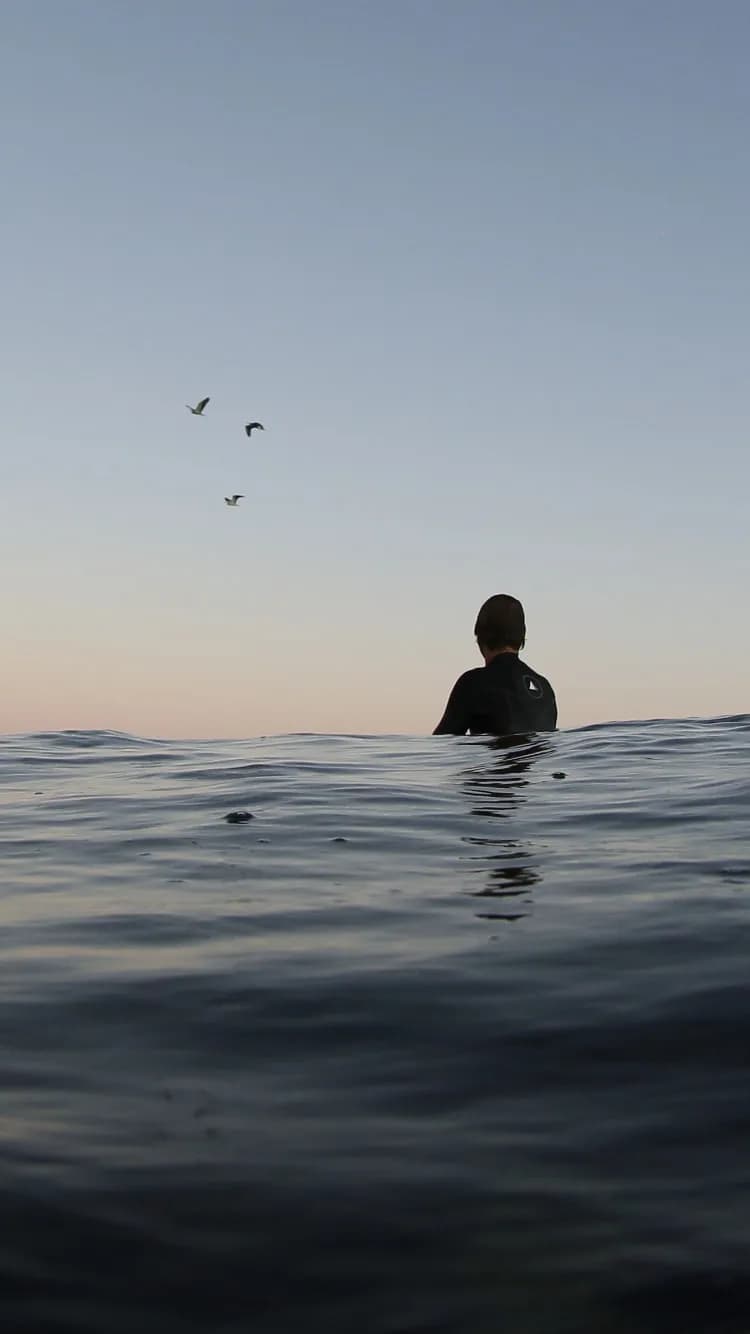 A person waiting in calm water beneath an open evening sky.