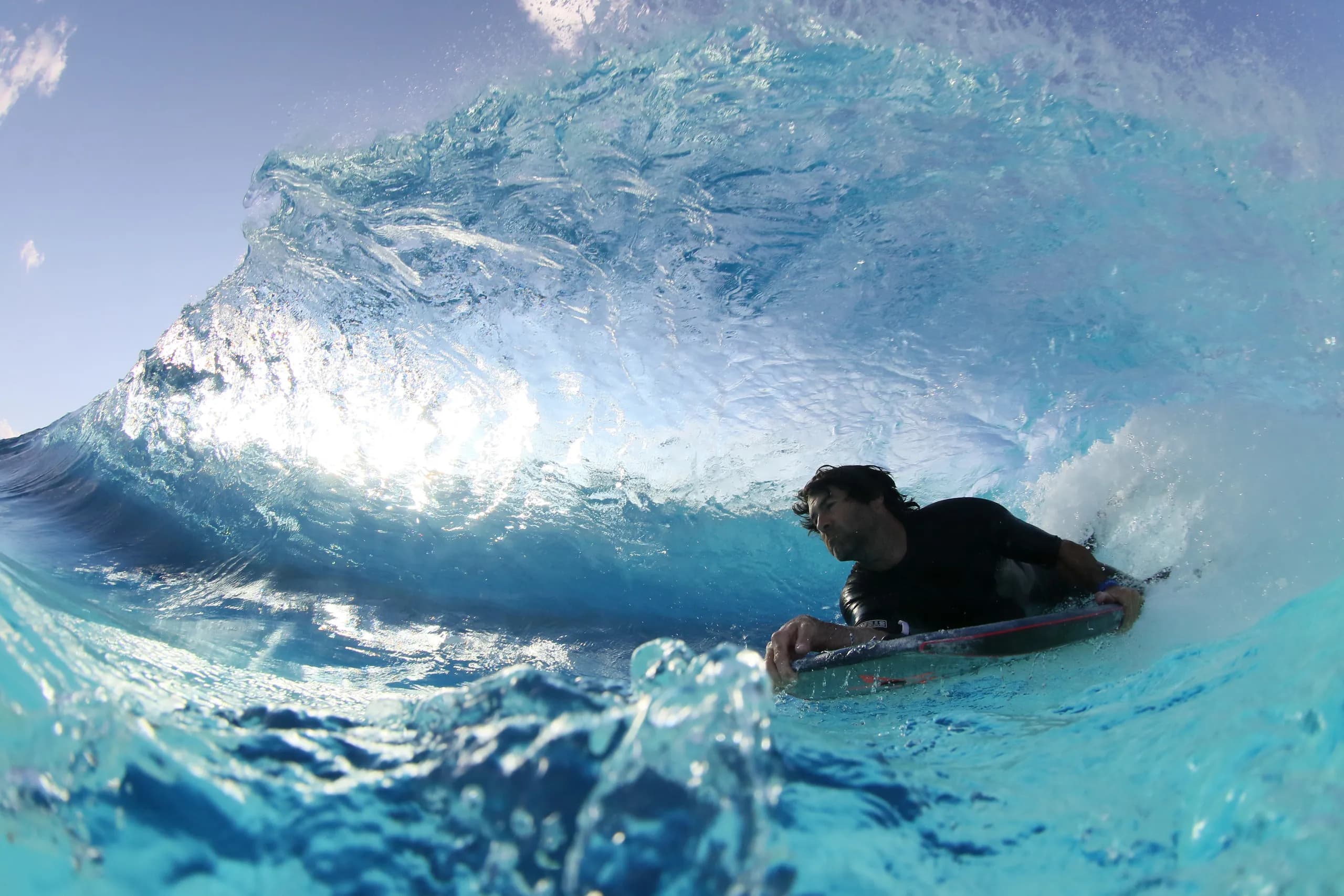 A bodyboarder moving through a bright blue breaking wave.