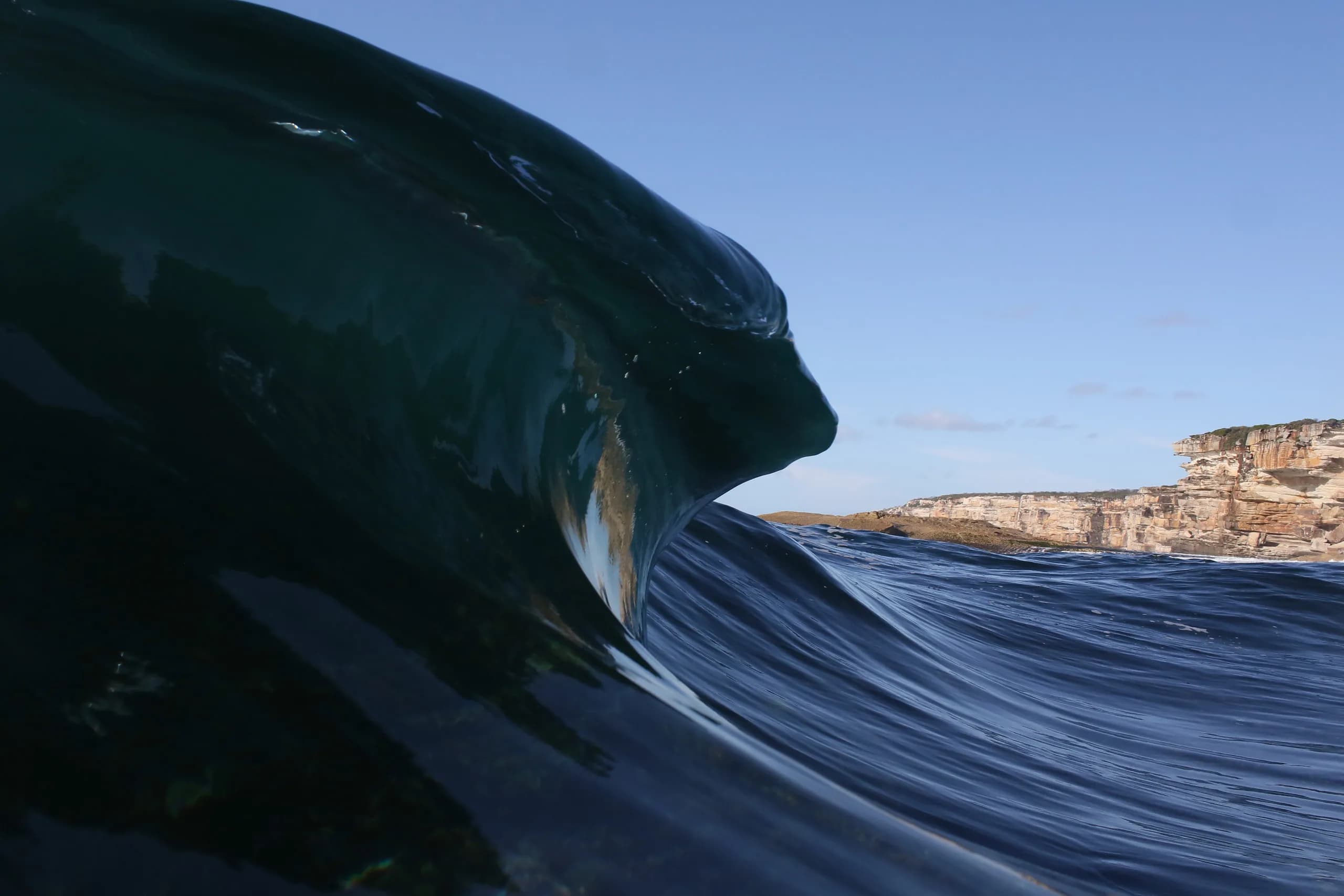 A dark blue wave curling toward a rocky shoreline.