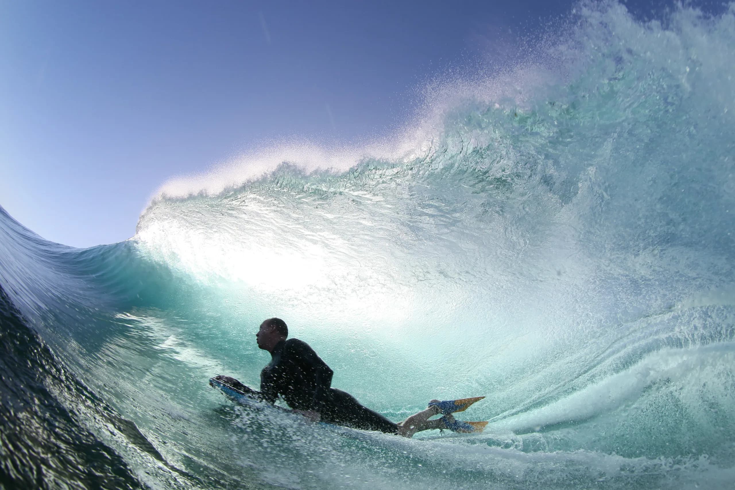 A bodyboarder driving through the base of a powerful blue wave.