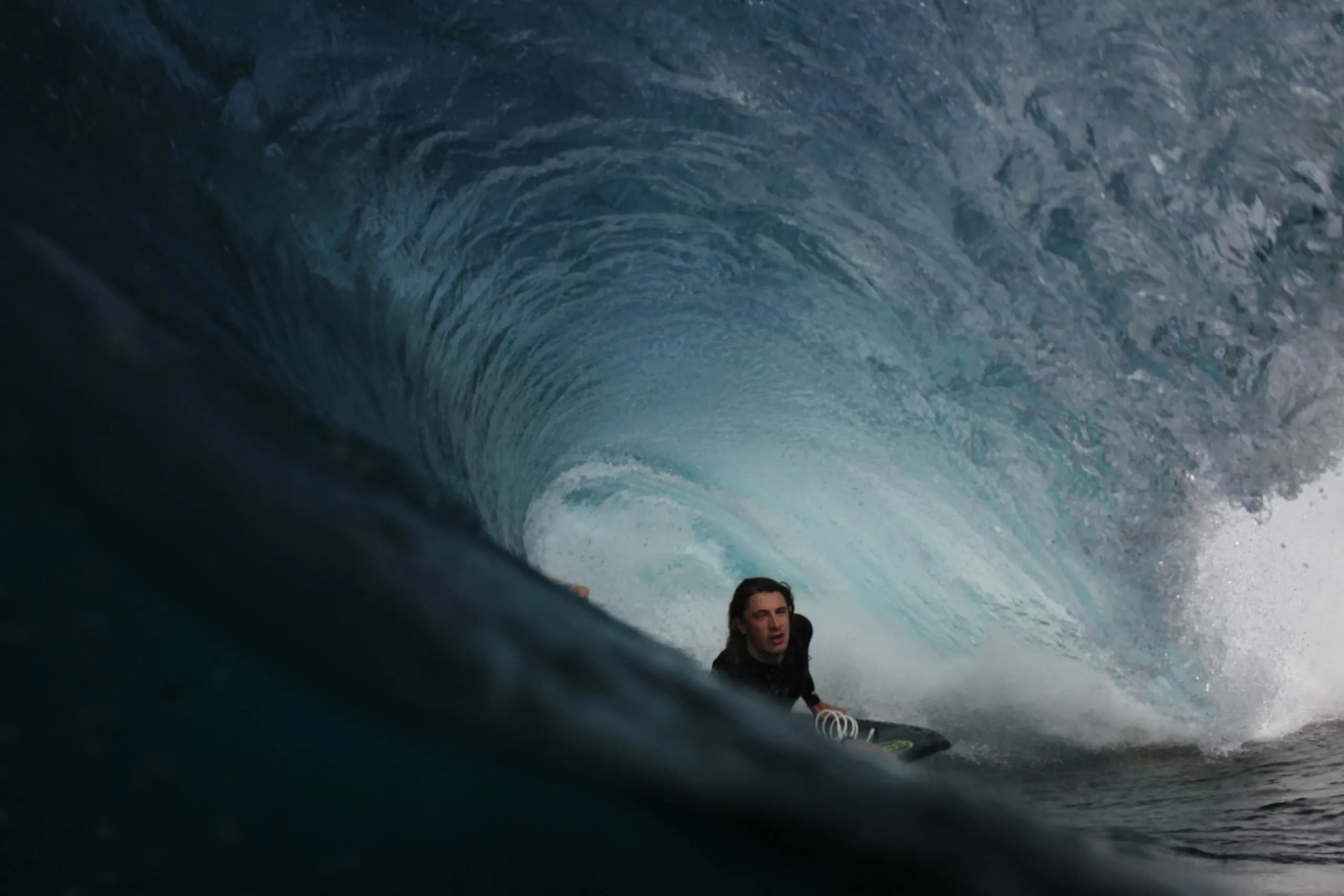 A surfer framed inside the curve of a dark blue wave.