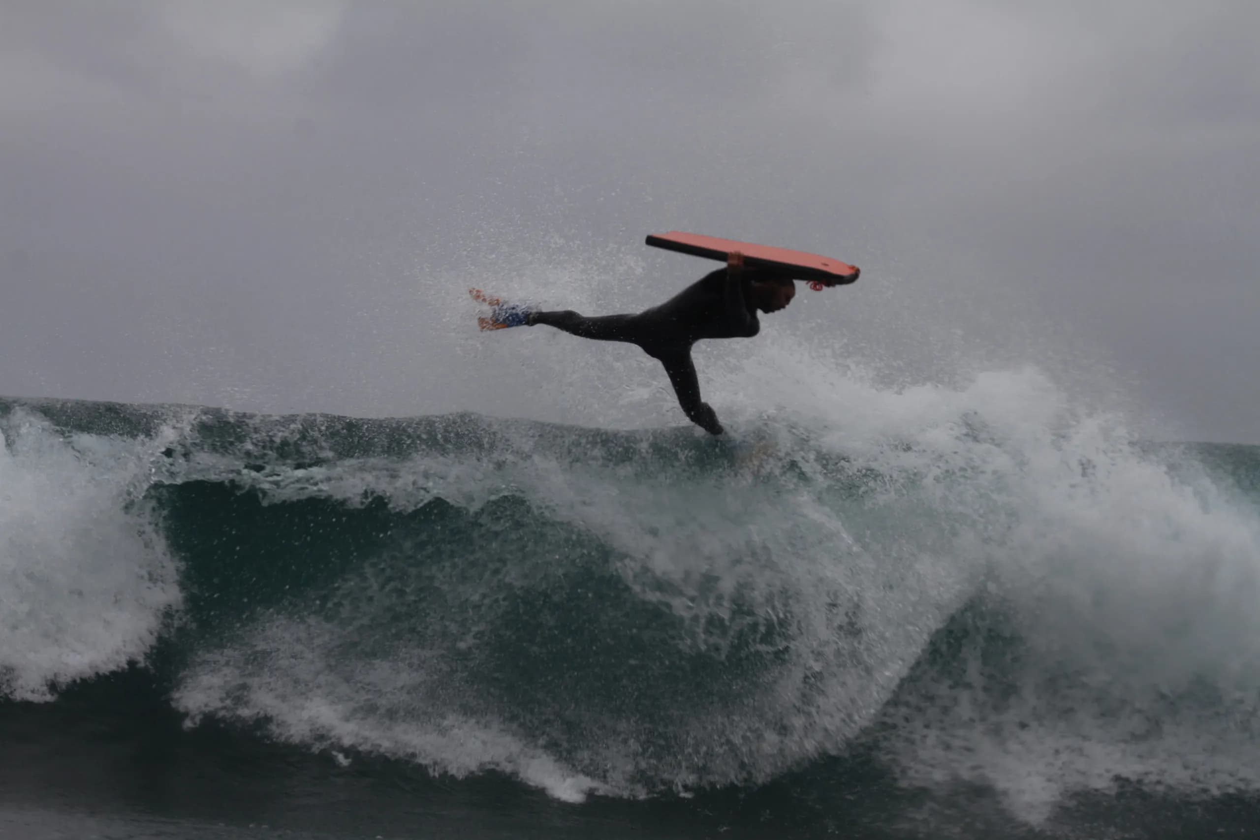 A bodyboarder and red board airborne above white water.
