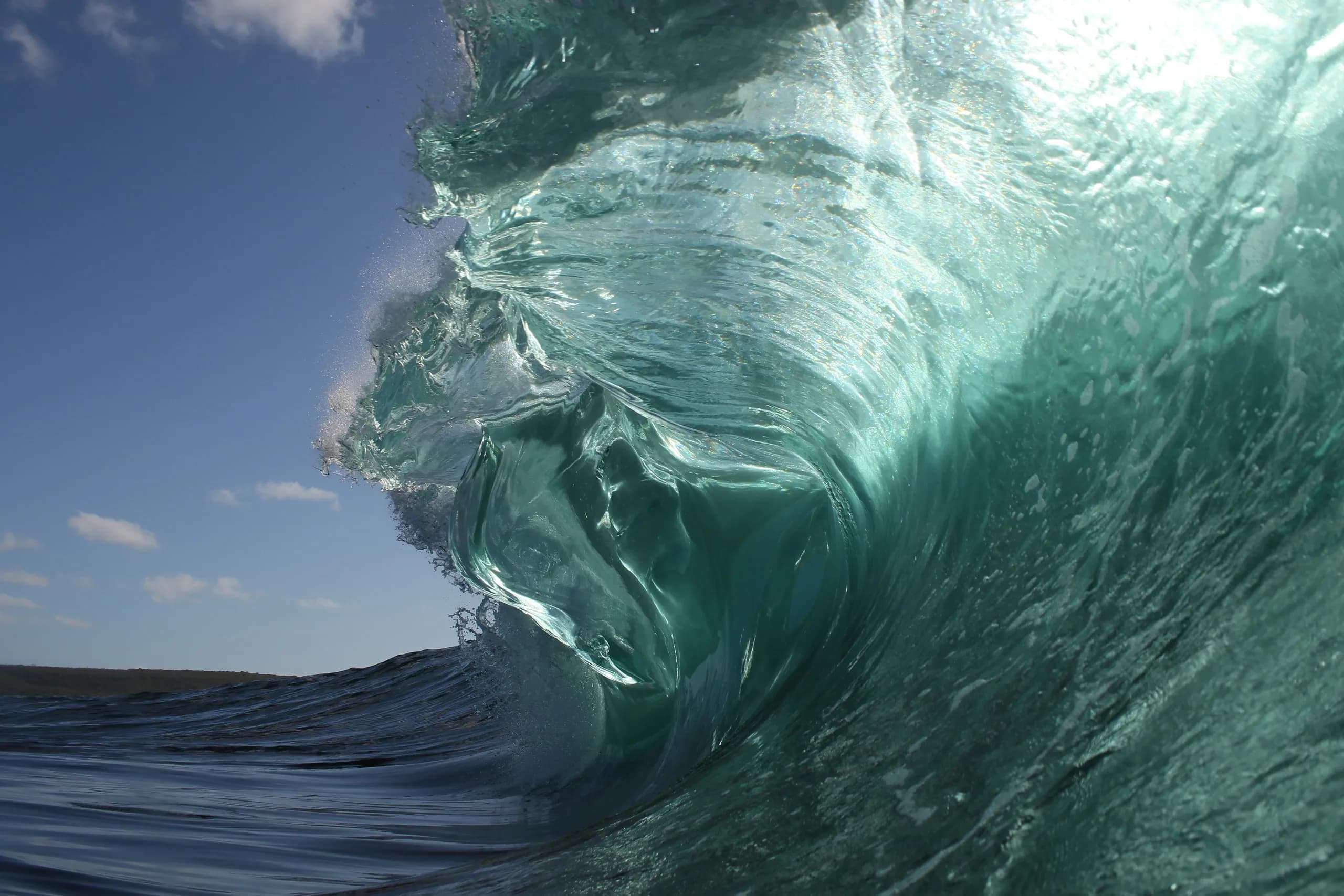 A translucent green wave lifting above open water.