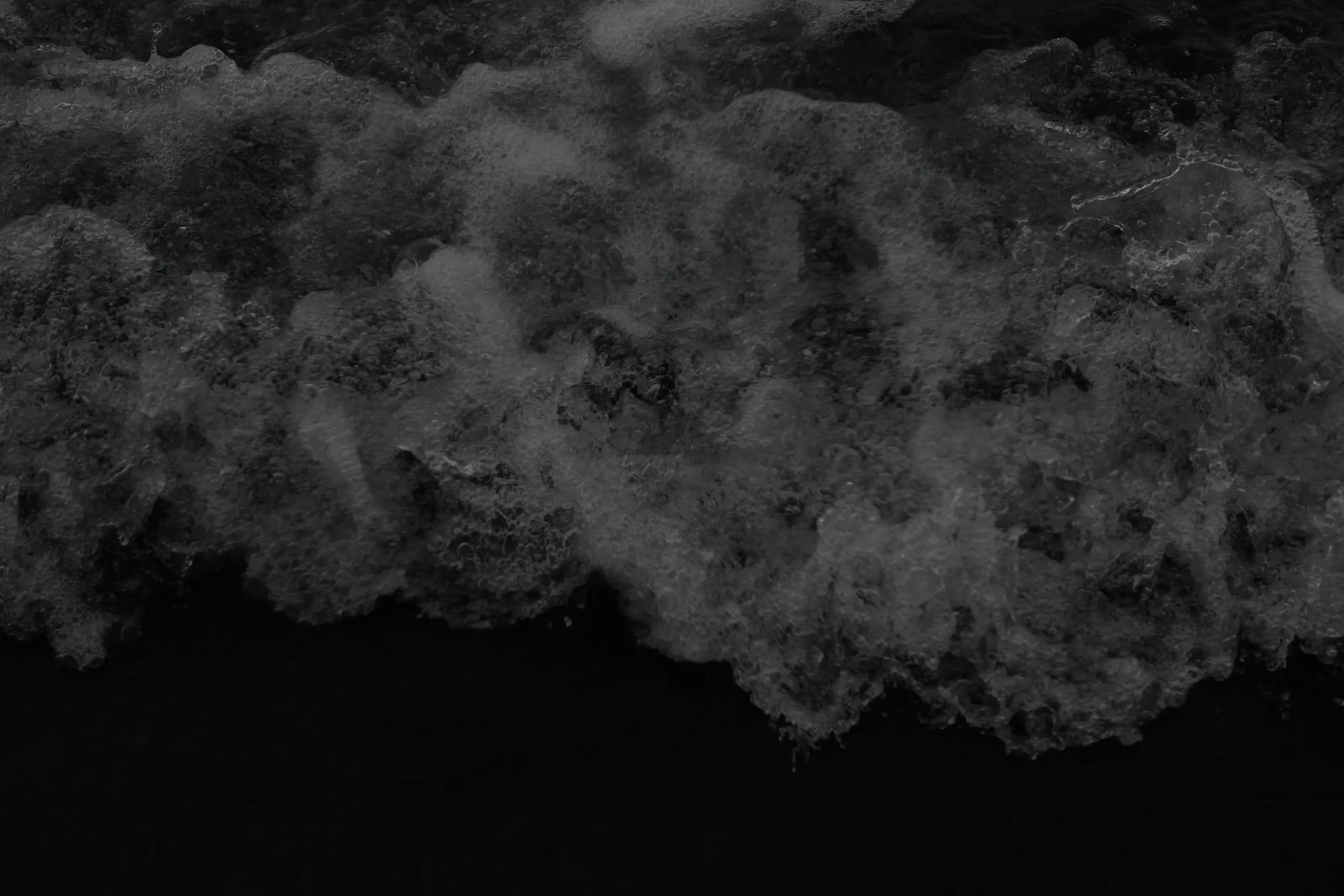 A dark aerial view of white water collapsing into the ocean.