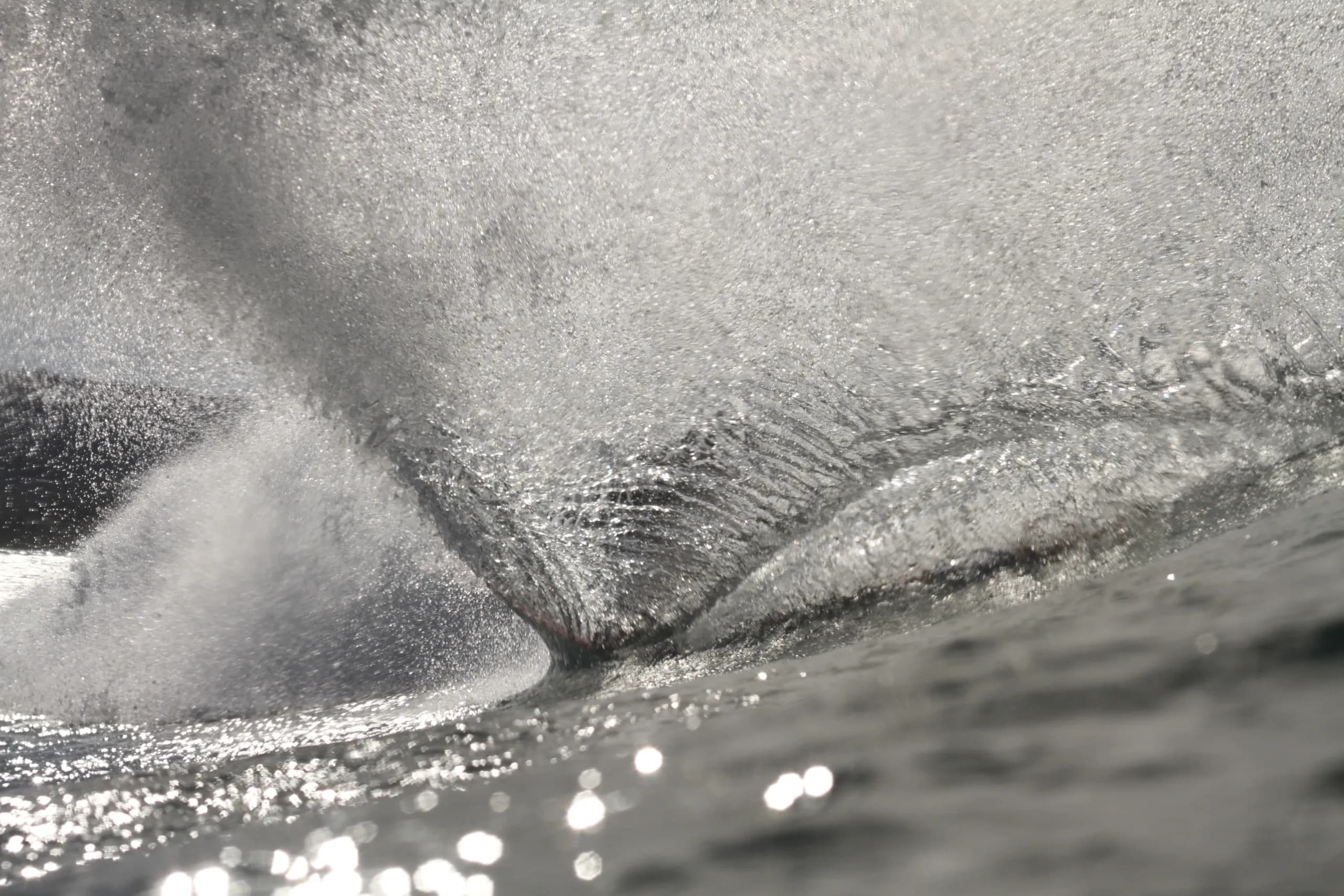 A monochrome view of spray and bubbles beneath a breaking wave.