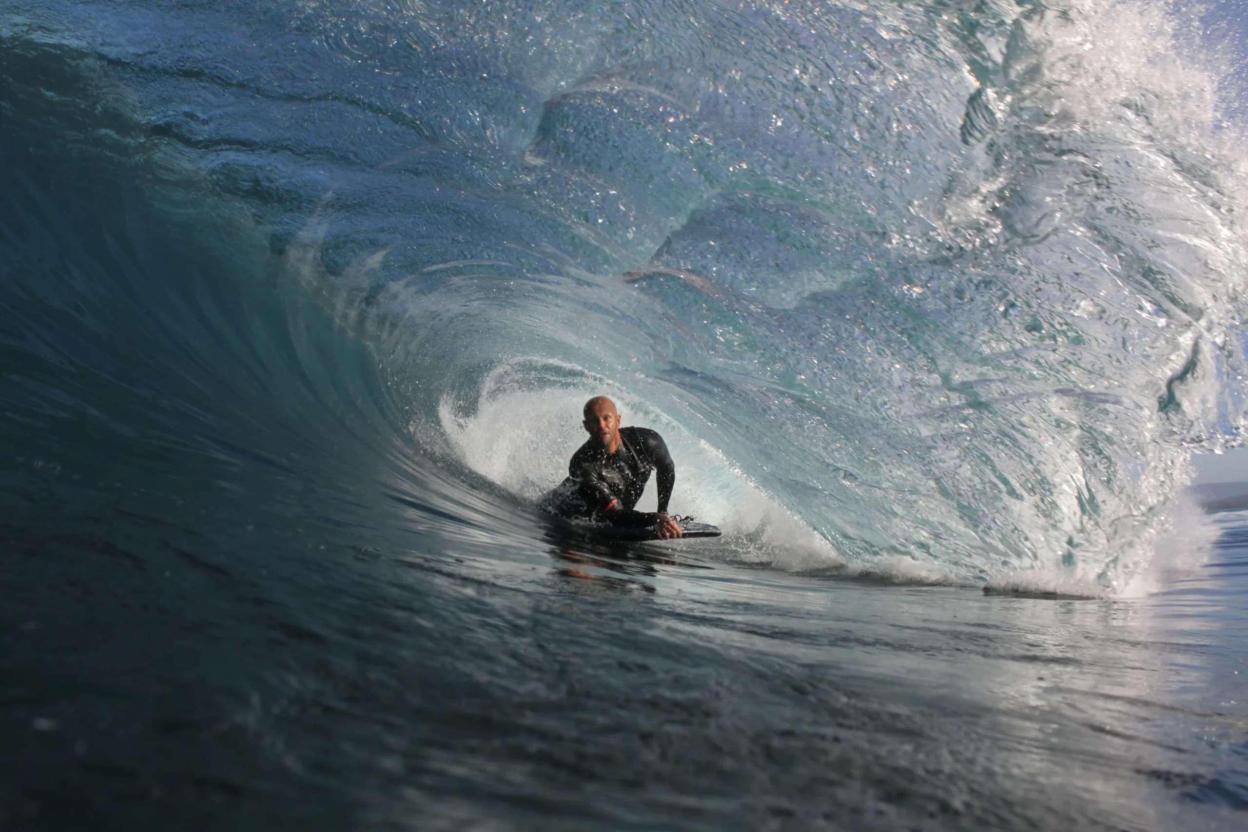 A bodyboarder riding within a textured blue barrel.