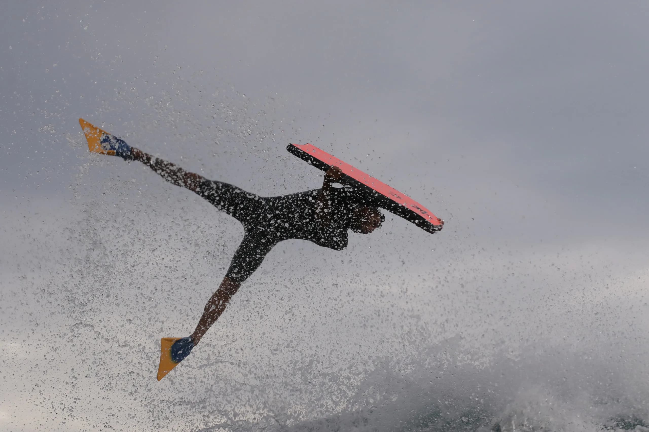 A bodyboarder airborne above the wave with a red board.