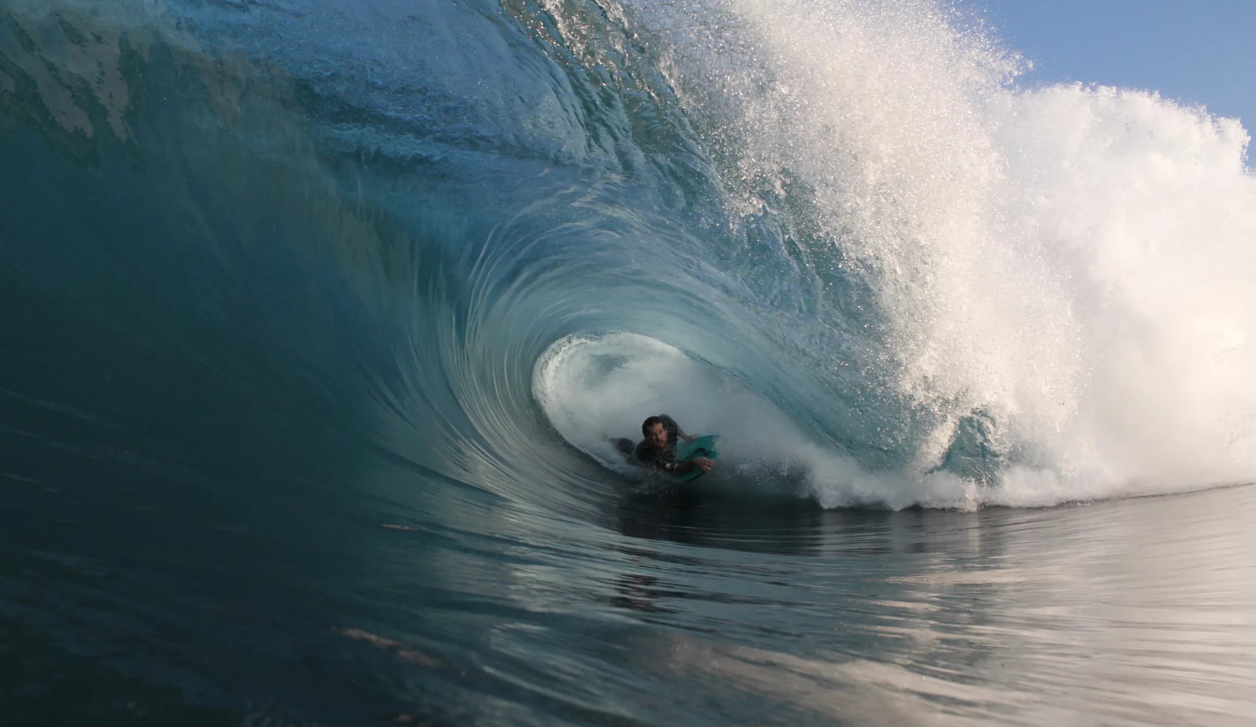 A bodyboarder holding a line beneath a large blue wave.
