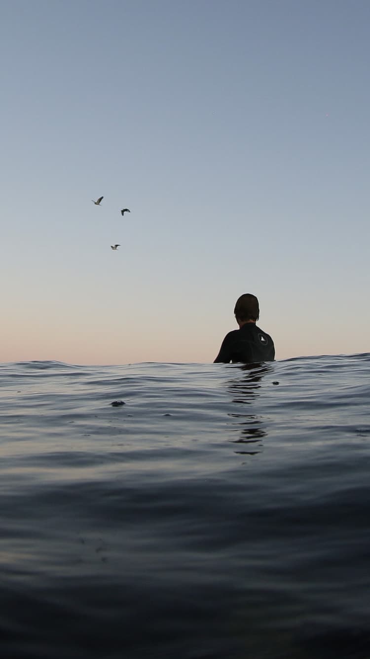 A person waiting in calm water beneath an open evening sky.