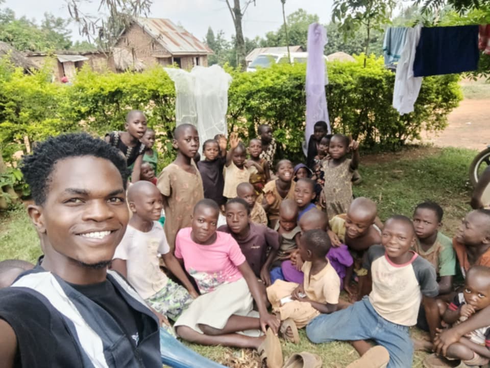 Magezi takes a group photograph with children gathered outdoors.